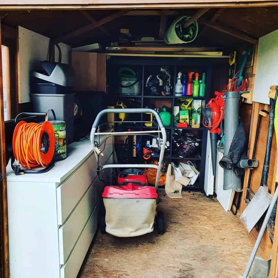 Inside a shed with neatly organized tools, lawnmower, shelves with garden supplies, and an orange extension cord reel