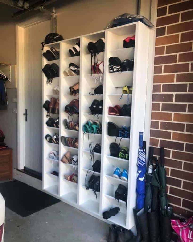 White shoe rack filled with neatly organized pairs of shoes, standing against a brick wall in a garage