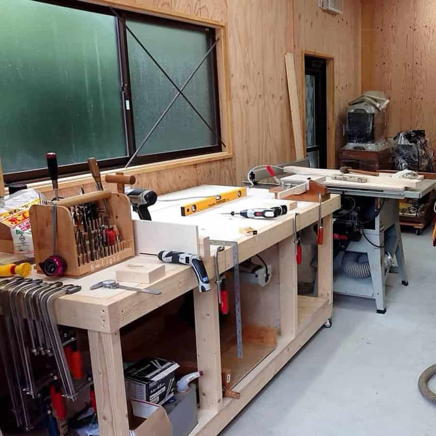 Woodworking shop with wooden workbenches, tools like clamps and drills, and a window with frosted glass