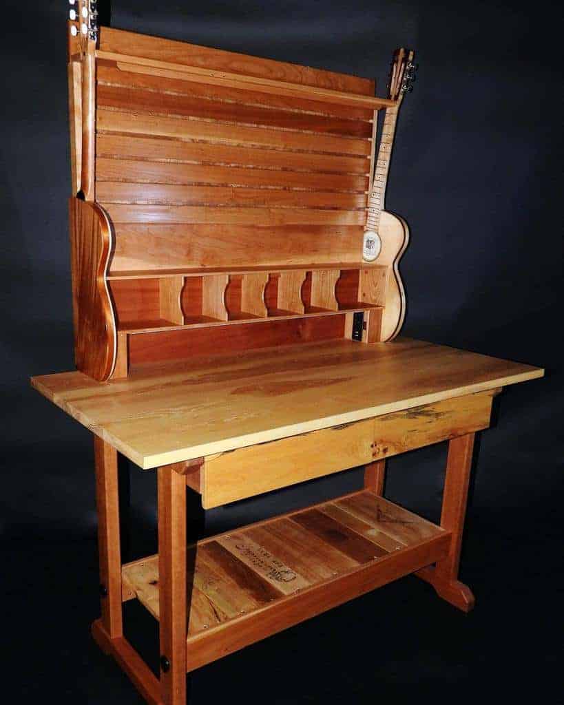 Wooden desk with guitars integrated into its design, featuring multiple slots and shelves, set against a dark background