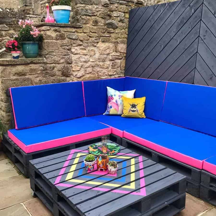 Vibrant outdoor pallet sofa set with bold blue and pink cushions, a geometric pallet coffee table, and colorful accent pillows