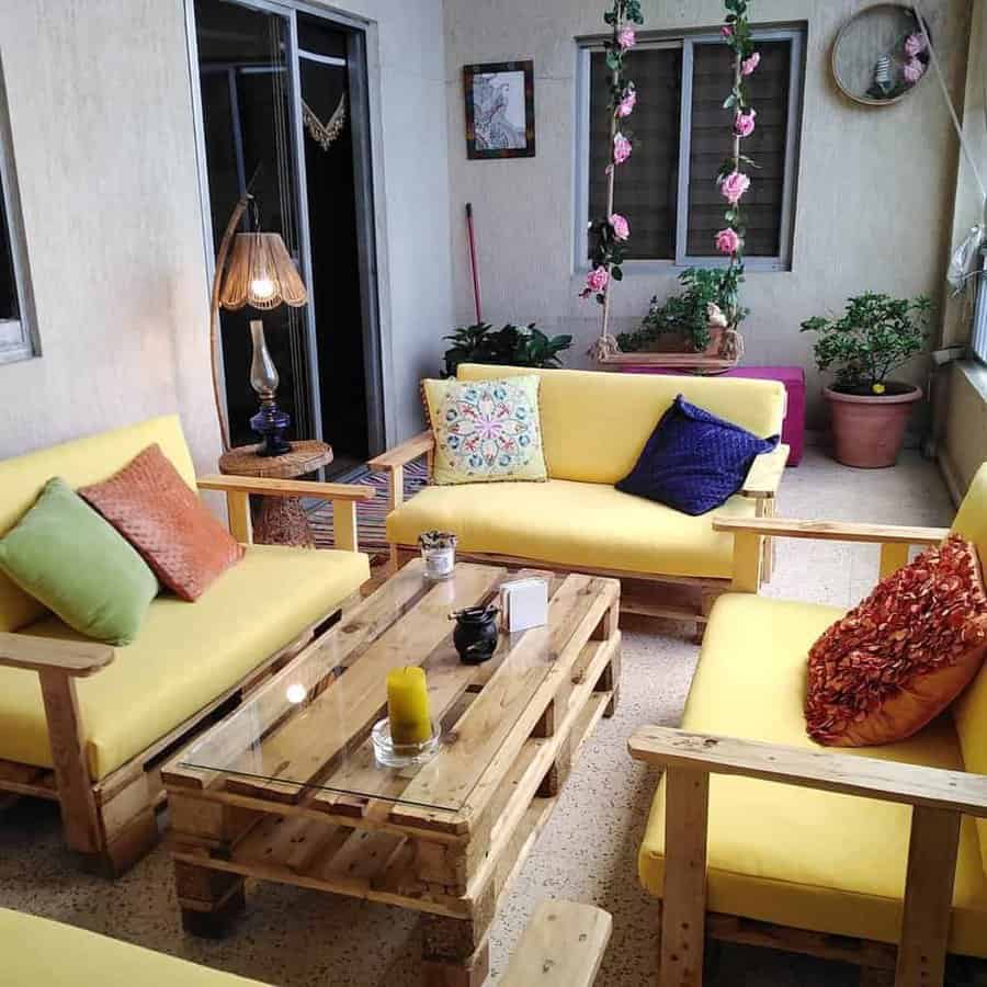 Indoor pallet sofa set with bright yellow cushions, colorful throw pillows, a glass-top pallet coffee table, and cozy decorative accents