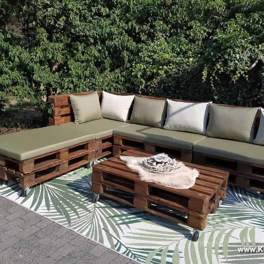 Outdoor patio with wooden pallet furniture, including a sectional sofa and coffee table, green cushions, and a tropical rug