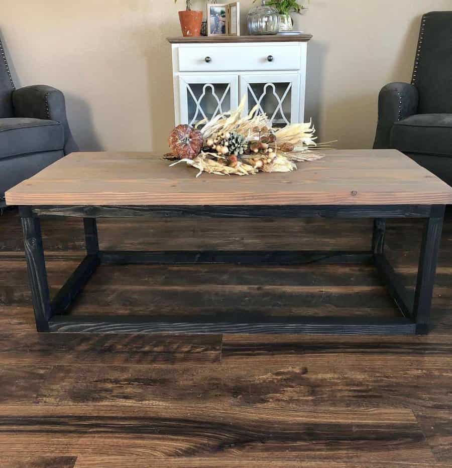 Wooden coffee table with a fall-themed centerpiece, surrounded by two gray chairs on a wooden floor