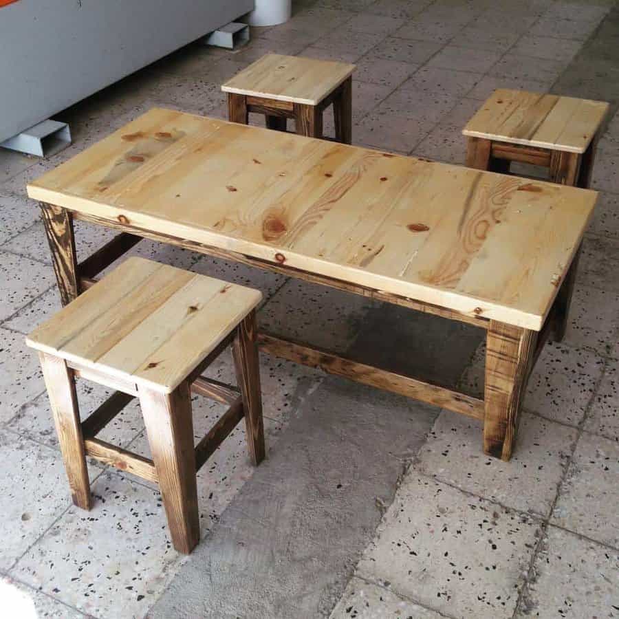 A wooden pallet table with four matching stools arranged around it on a tiled floor