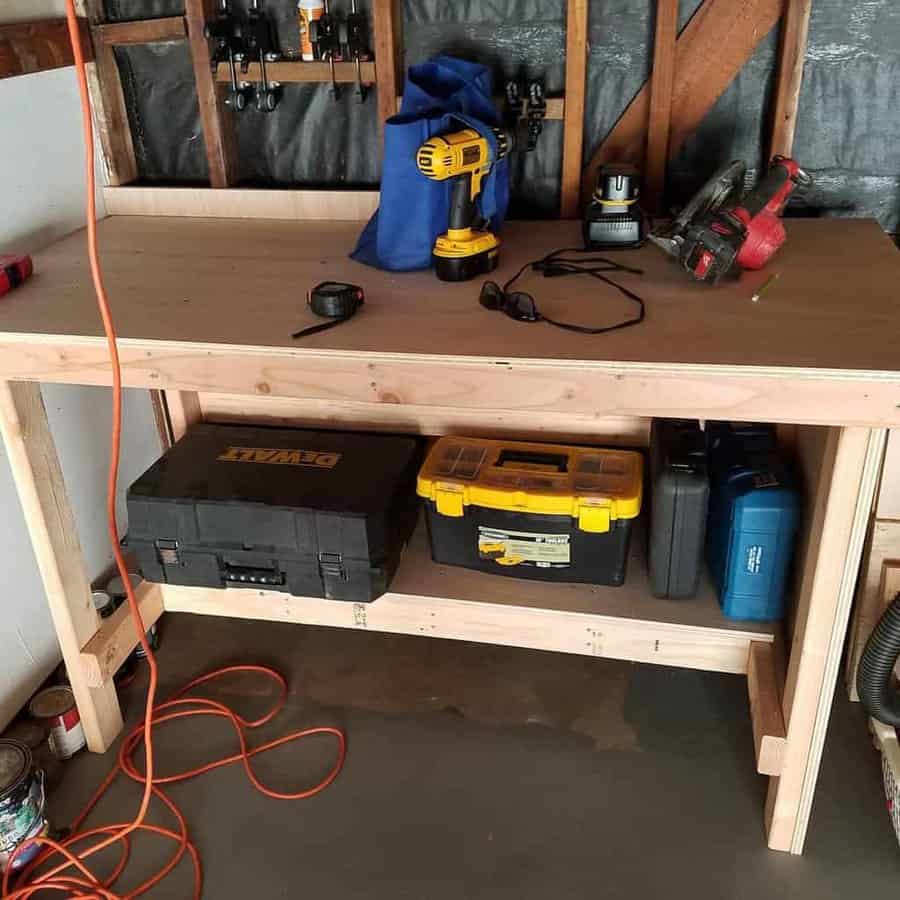 Wooden workbench with power tools, tape measure, safety glasses, and toolboxes; an extension cord is plugged in the corner