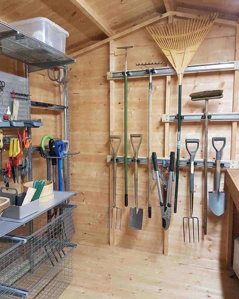 Organized shed with various garden tools hanging on walls, including shovels and rakes; shelves hold baskets and garden accessories