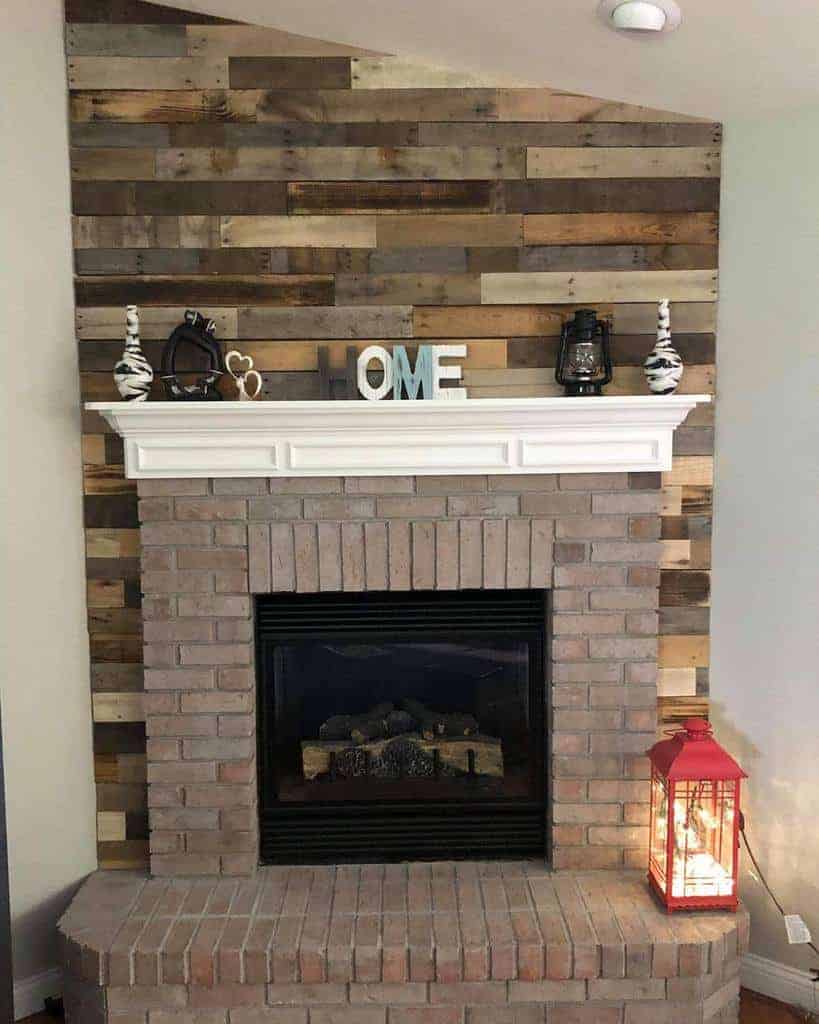 Brick fireplace with a rustic wooden pallet backdrop, decorated with lanterns, vases, and "LOVE" letters on the mantel, and a red lantern