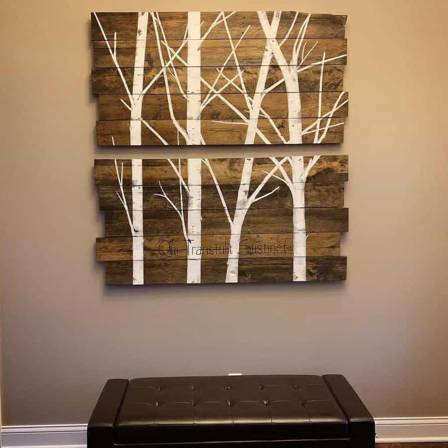 Wall art of tree branches painted on wooden panels above a brown bench against a beige wall