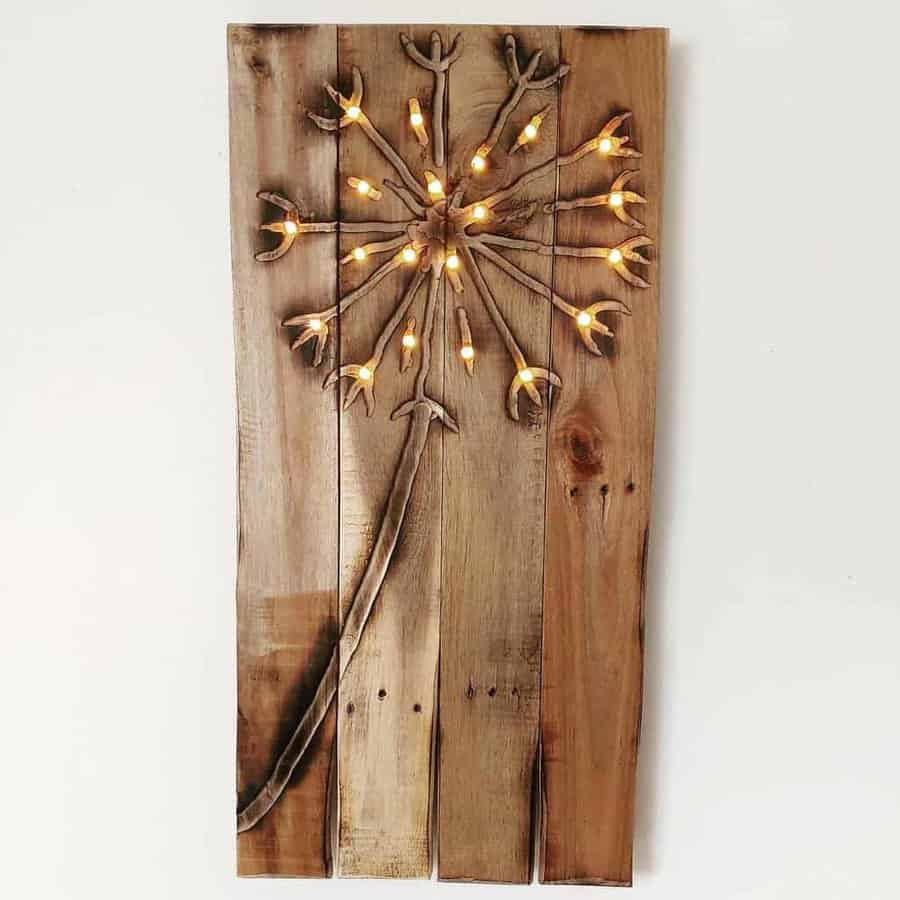 Wooden wall art of a dandelion with embedded yellow lights resembling seeds, on a rustic wooden plank background