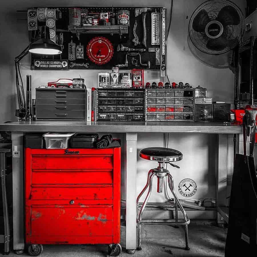 Mechanic's organized workspace with a red tool chest, metal stool, wall clock, and various tools on pegboard in grayscale