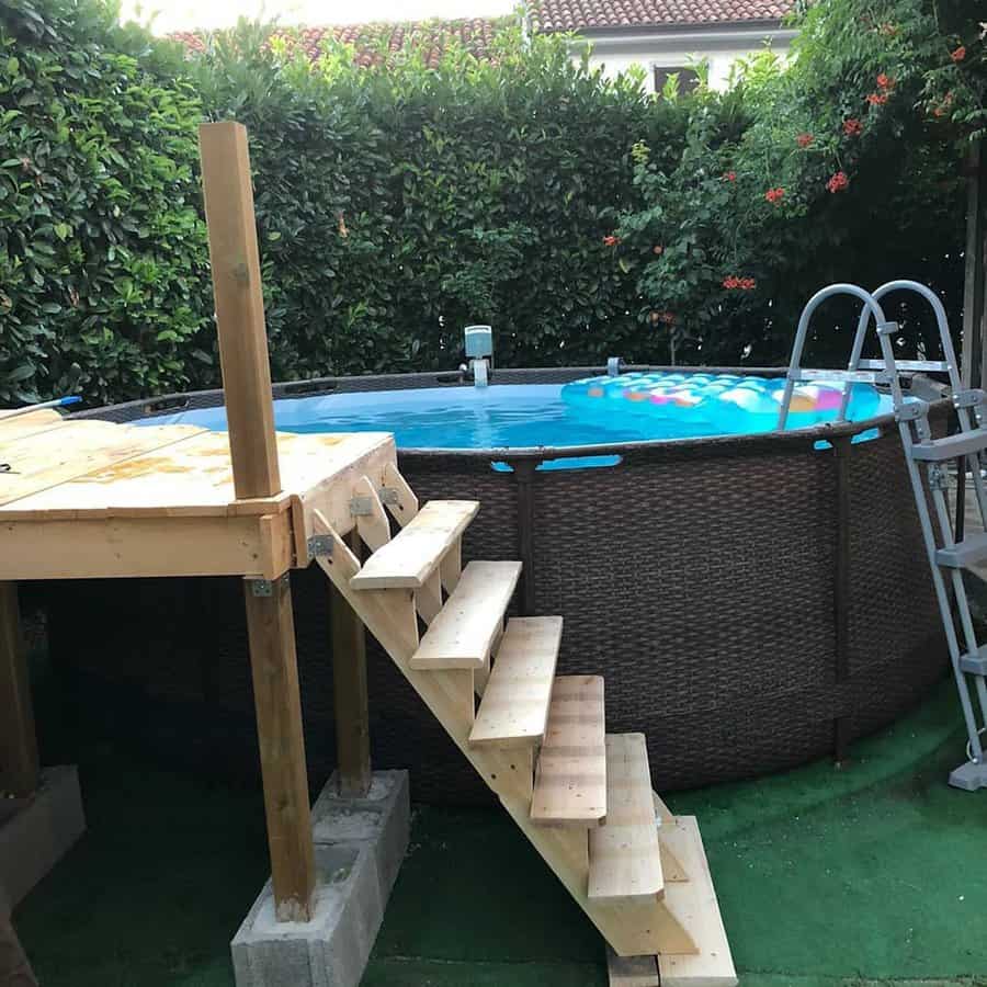 Round above-ground pool with a wooden deck and ladder, surrounded by greenery, inflatable float in the water