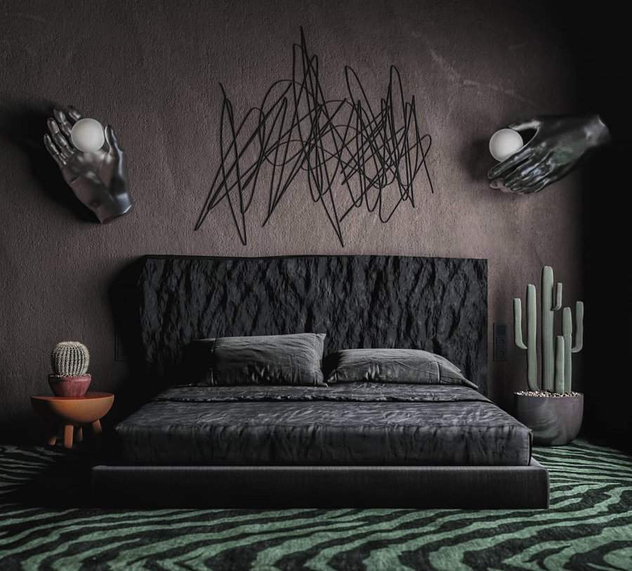 A black, modern bedroom with abstract wall art, unique hand-shaped sconces, a cactus plant, and a zigzag-patterned green carpet