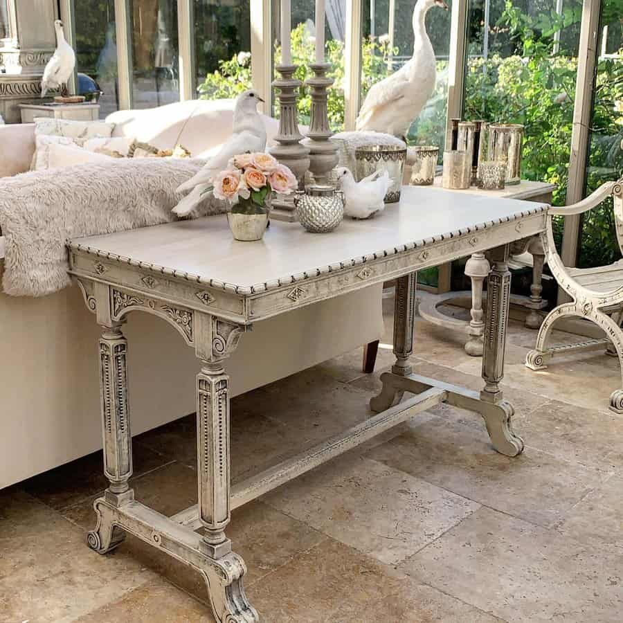 Elegant antique-style table with a distressed white finish, decorated with candles, roses, and doves in a bright conservatory setting.