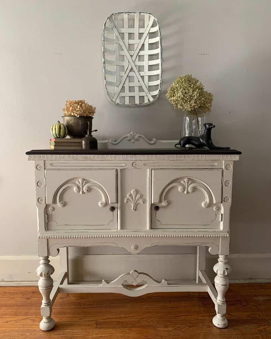 Vintage sideboard painted in distressed white with ornate carvings, styled with dried flowers, a decorative tray, and rustic accents