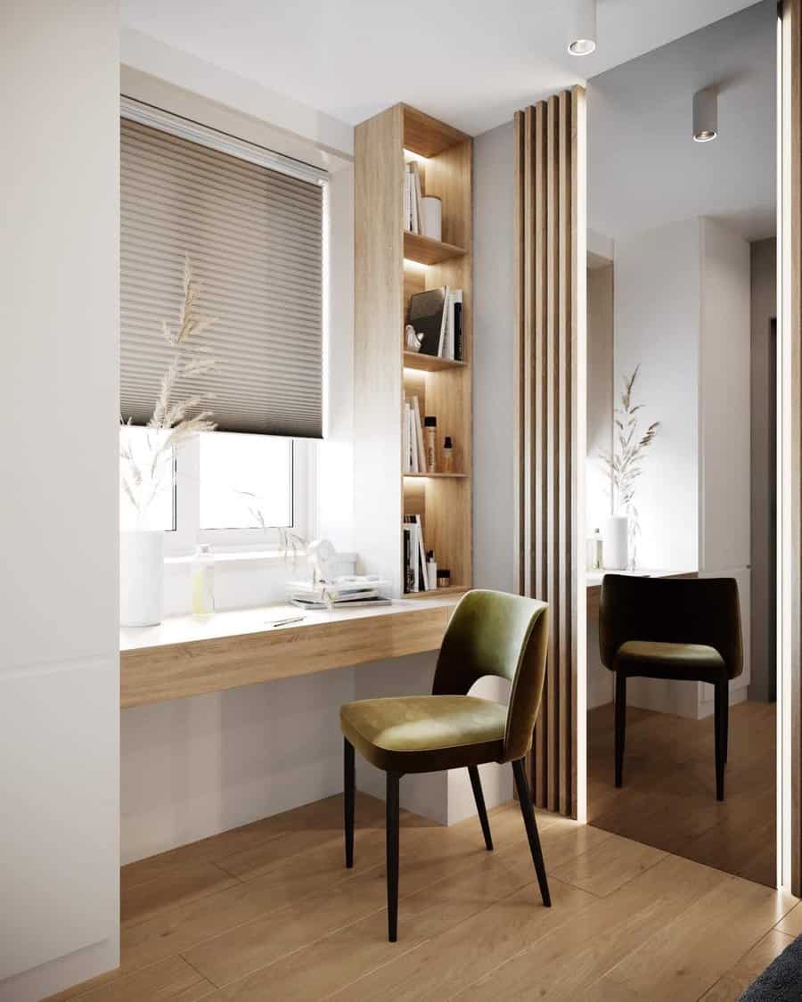 Minimalist bedroom office with a floating wood desk, built-in shelves, and a velvet chair, complemented by a large mirror and soft lighting