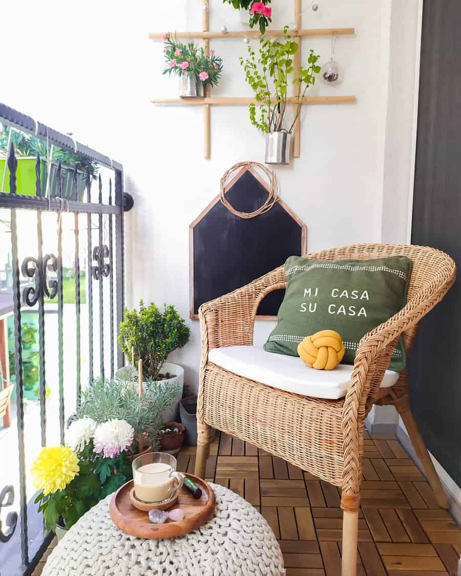 Cozy small balcony with a wicker chair, green cushion, plants, and a knitted pouf with tea, creating a relaxing outdoor nook