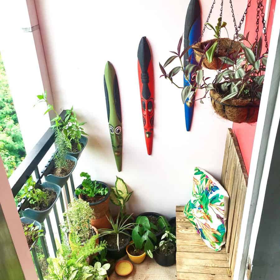 Lush small balcony with potted plants, hanging baskets, tribal wall masks, and a wooden bench with a tropical cushion