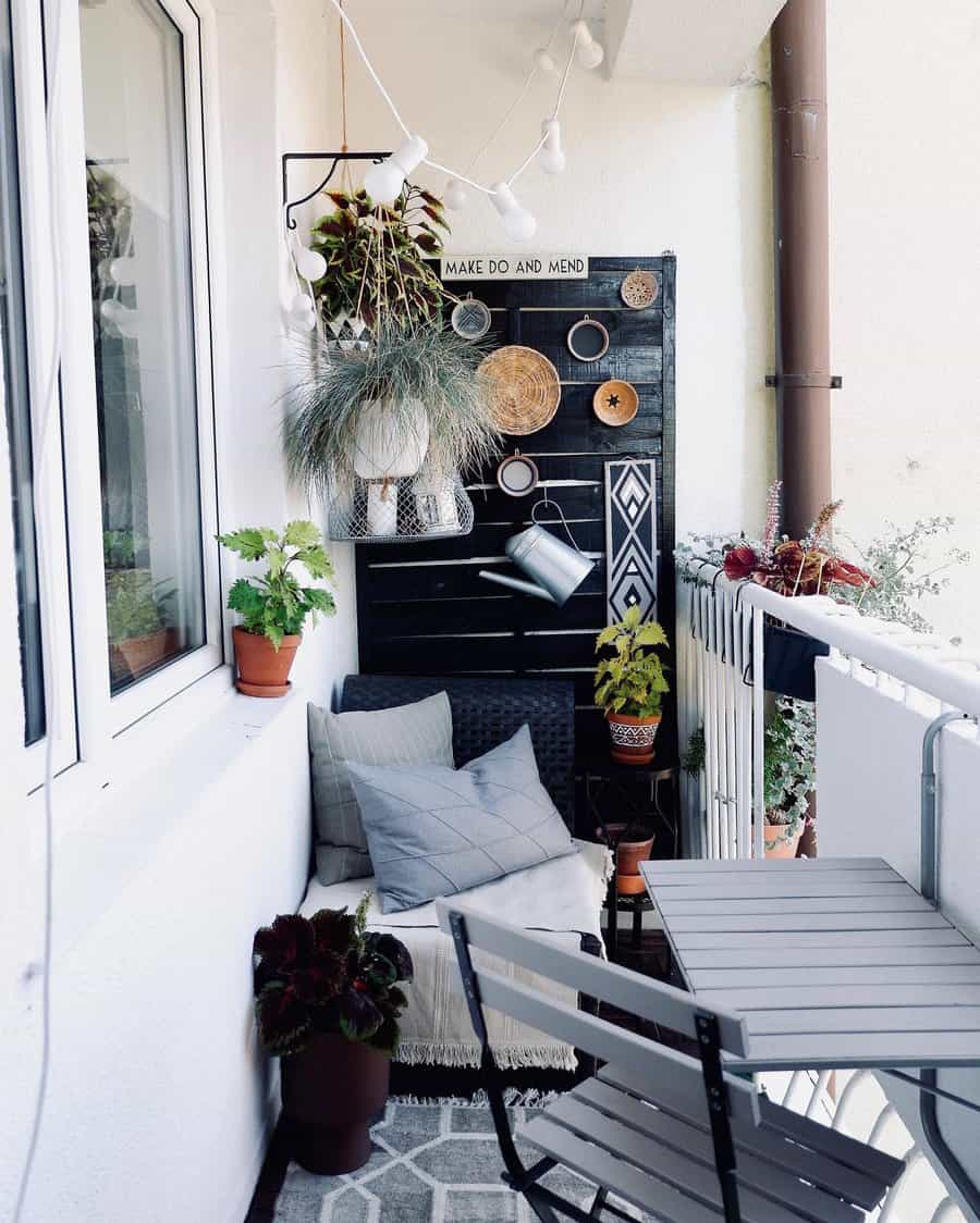 Chic small balcony with a cozy seating nook, potted plants, string lights, a black accent wall with decor, and a foldable table set