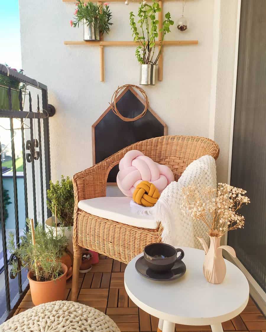 Cozy small balcony with a wicker chair, soft knit pillows, potted plants, a white side table with coffee, and warm natural decor