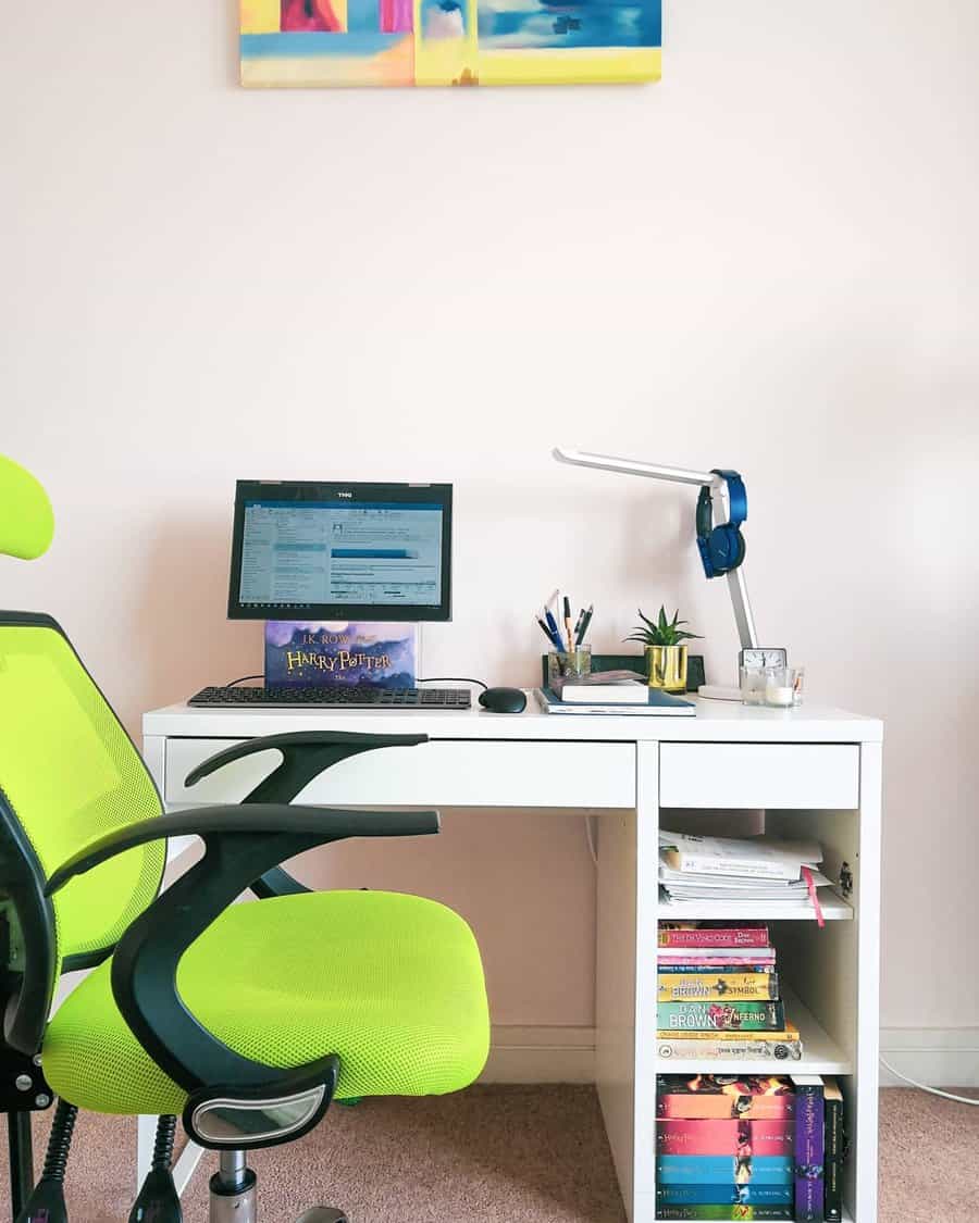 A home office with a green chair, white desk, laptop, desk lamp, books, and plant