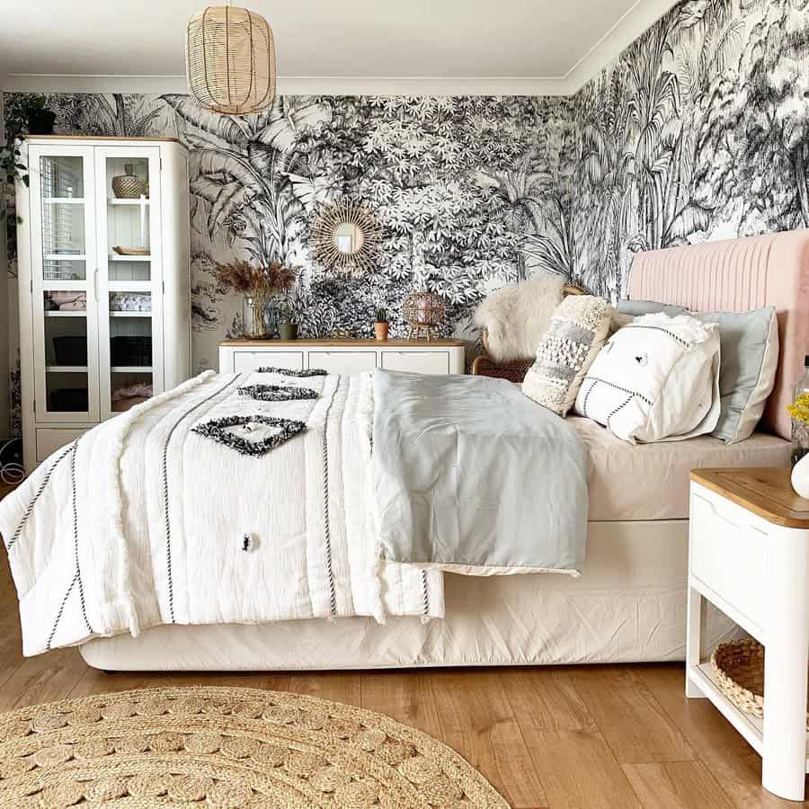 A cozy bedroom with a bed, patterned duvet, botanical wallpaper, wooden floor, woven rug, and decorative pillows