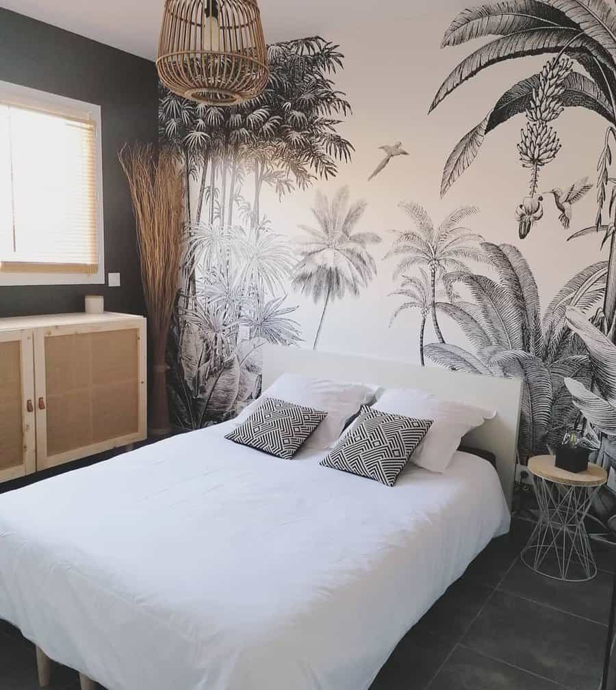 A bedroom with a tropical-themed wall mural, a white bed, patterned pillows, wicker pendant light, and a light wooden sideboard