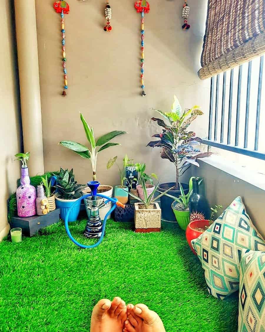 Relaxing small balcony with artificial grass, potted plants, colorful decor, patterned cushions, and a hookah for a cozy boho vibe