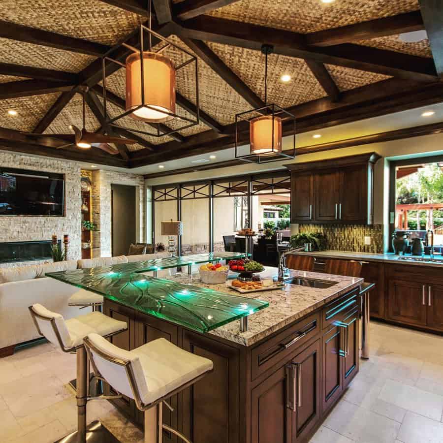 Luxurious kitchen with a glass breakfast bar attached to the island, featuring under-lighting, wooden cabinetry, and modern seating