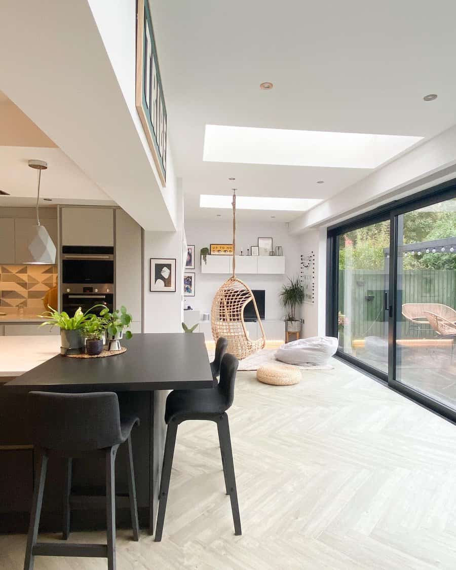 Modern kitchen with a sleek black breakfast bar attached to the island, complemented by dark barstools, indoor plants, and natural light