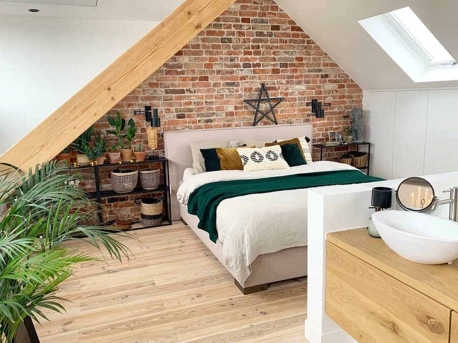 Modern attic bedroom with an exposed brick accent wall, warm wood tones, and lush greenery. Cozy textiles add a stylish and inviting touch.