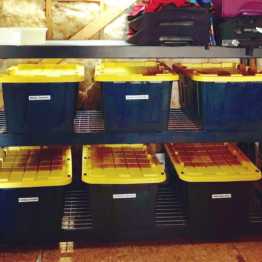 Labeled plastic storage bins with yellow lids neatly arranged on metal shelves in an attic, maximizing space and organization.