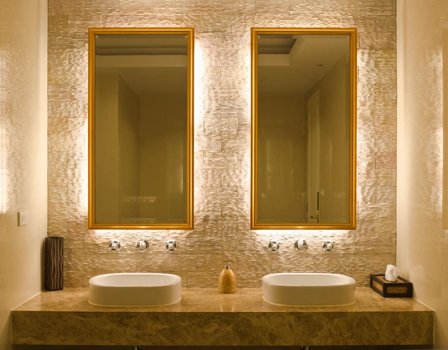 A modern bathroom with two illuminated mirrors, two sinks, and decorative tiles