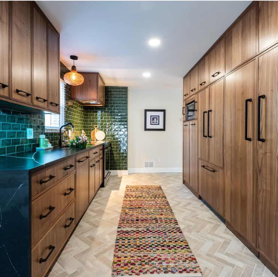 Galley kitchen with wooden cabinets, green tile backsplash, and patterned runner rug