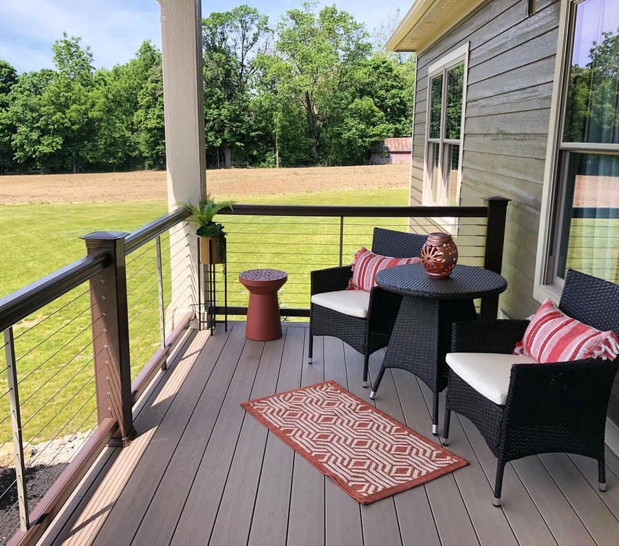 Small outdoor balcony with wicker furniture, striped cushions, and a modern railing, offering a cozy spot with a scenic countryside view