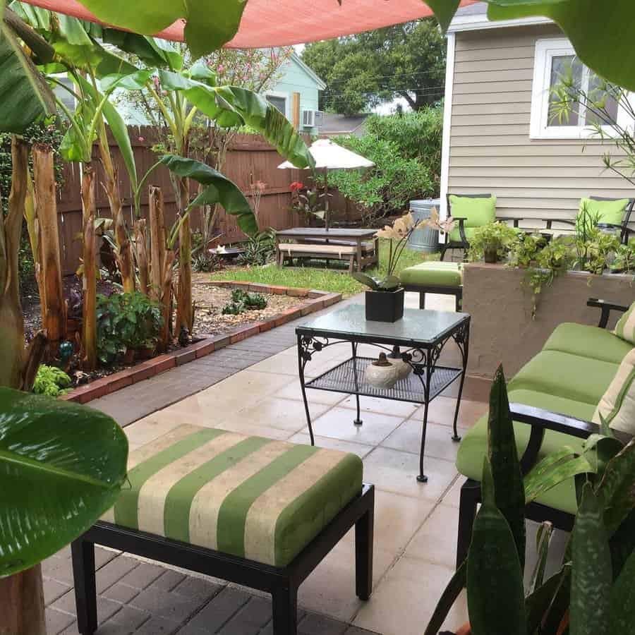 Lush Florida backyard with tropical plants, banana trees, and cozy green patio seating under a shade sail for a relaxing outdoor retreat