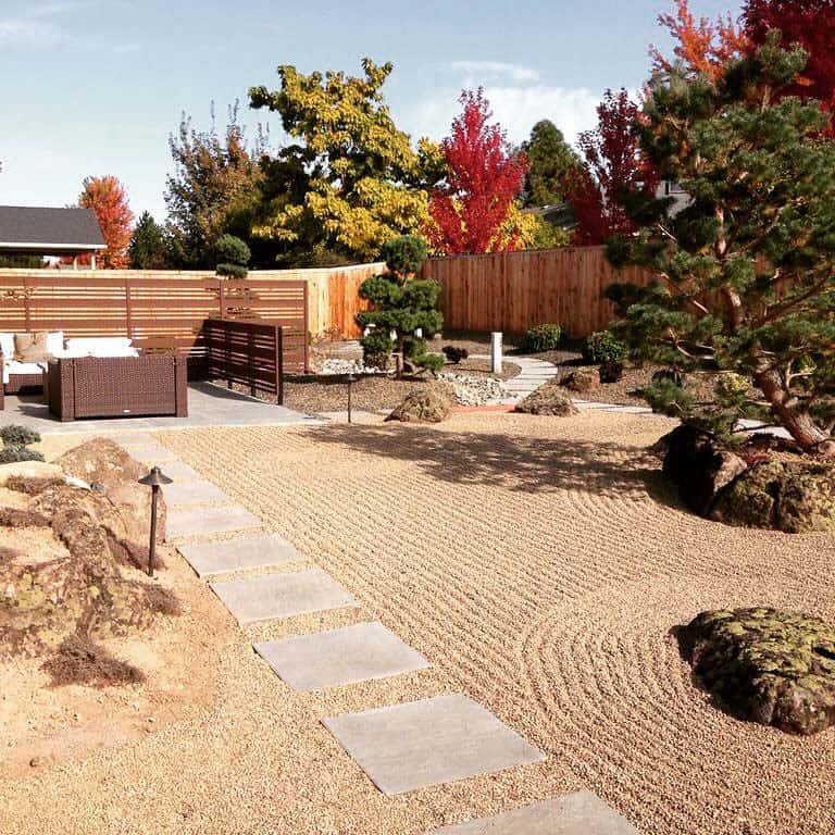 A serene Japanese-style backyard with raked gravel, stepping stones, sculpted evergreens, and vibrant autumn foliage