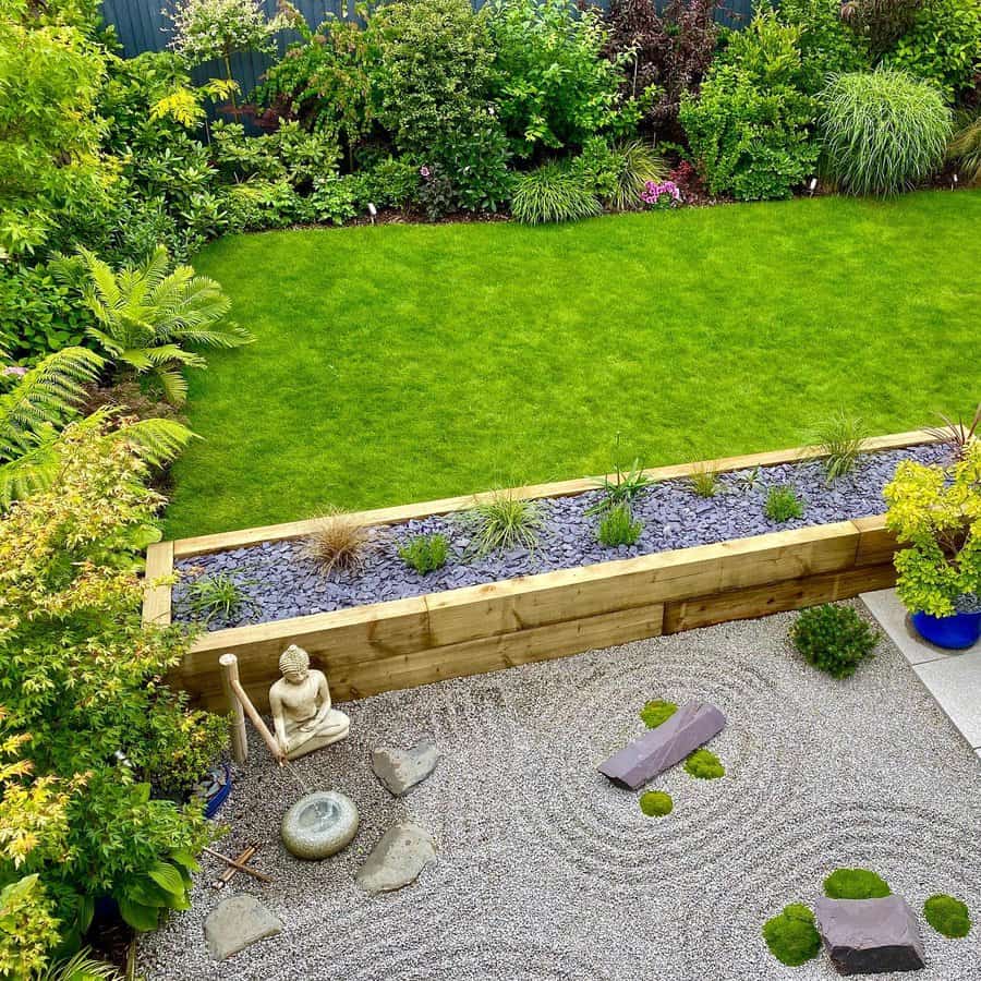 Aerial view of a garden with a grass lawn, gravel zen garden, wooden planter, stone decorations, and a Buddha statue