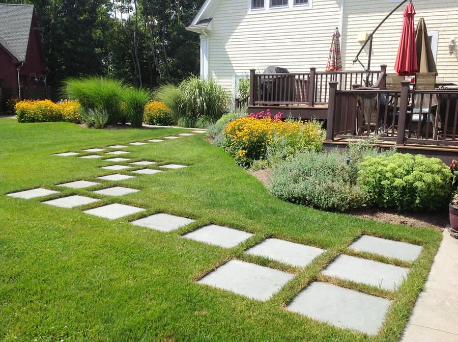 Backyard with low-maintenance landscaping featuring stepping stone pathway, vibrant flower beds, and a cozy wooden deck