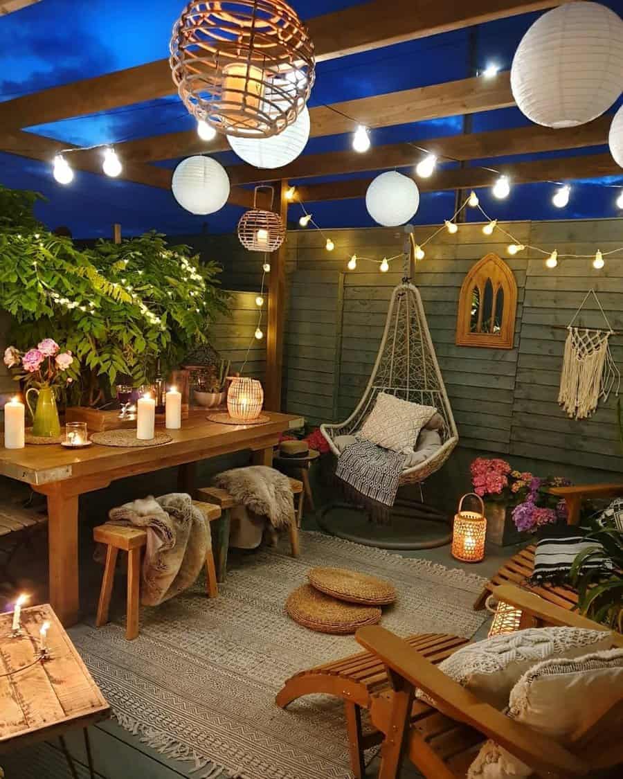 Cozy outdoor patio with string lights, candles, a wooden table with chairs, hanging chair, and lush greenery