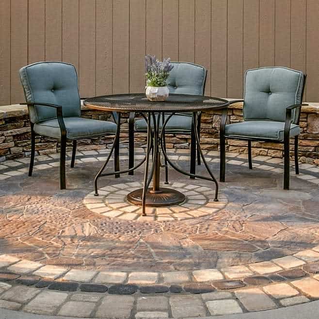 Patio set with a round table and three upholstered chairs on a stone surface, with a small plant on the table