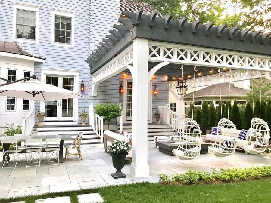 Charming pergola-covered patio with hanging chairs, string lights, and a cozy outdoor dining area shaded by a large umbrella