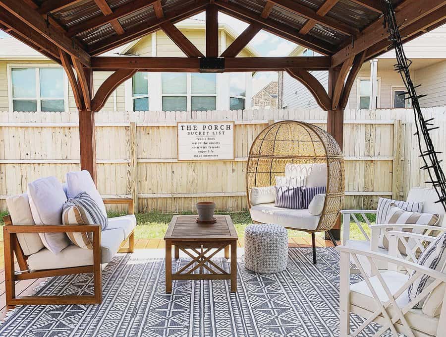 Charming wooden gazebo with cozy seating, a rattan egg chair, patterned rug, and a rustic coffee table for a stylish shaded backyard retreat