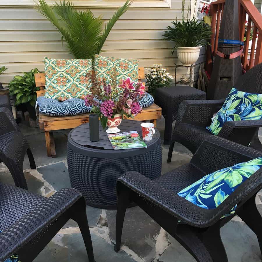 Cozy patio with wicker chairs, floral cushions, round table with flowers, plants, and a loveseat with patterned pillows