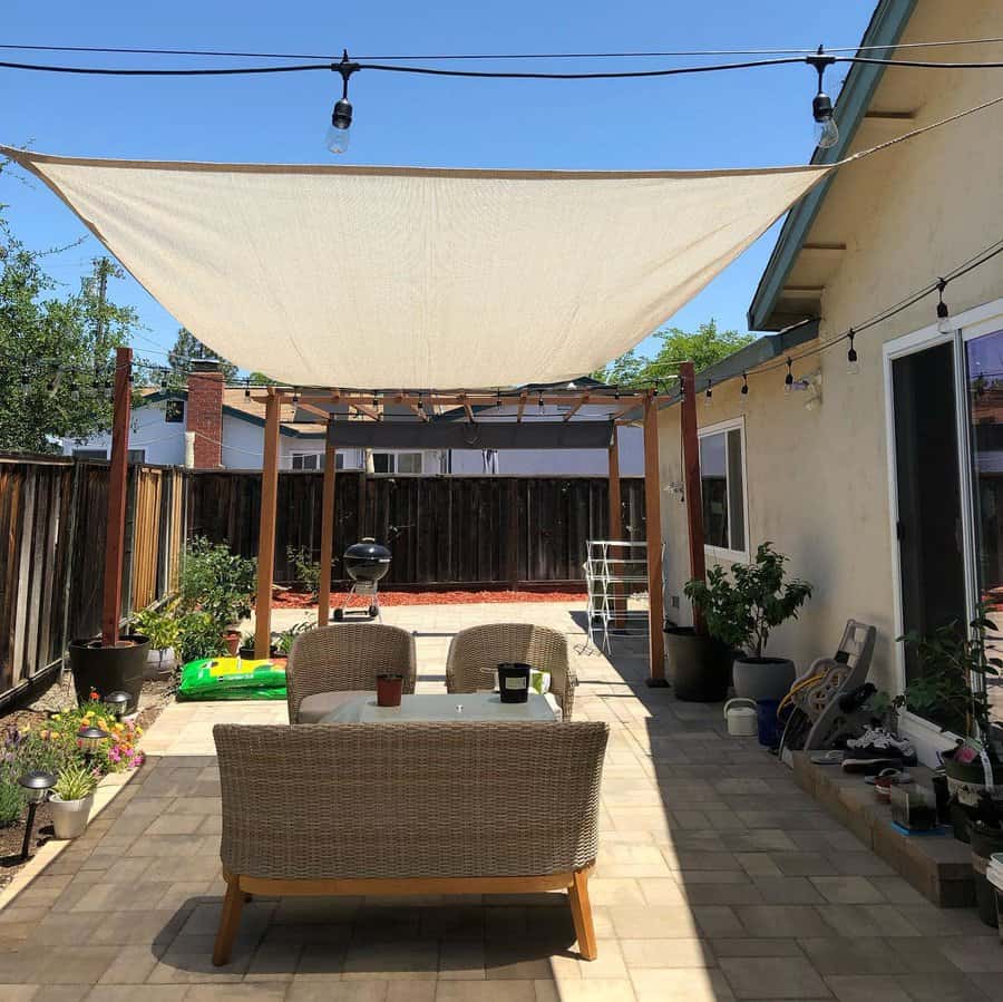 Modern backyard patio with a large shade sail, wicker seating, string lights, and a pergola, creating a stylish outdoor retreat