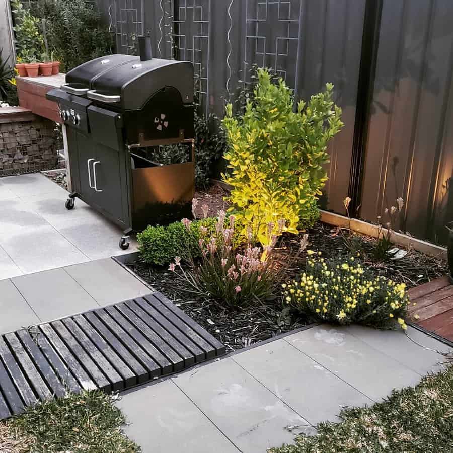 Modern backyard landscaping with a sleek black BBQ grill, illuminated plants, and a mix of stone and wood pavers for a cozy outdoor vibe