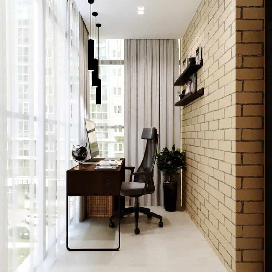 Enclosed balcony transformed into a stylish home office with a sleek desk, ergonomic chair, exposed brick wall, and floor-to-ceiling windows