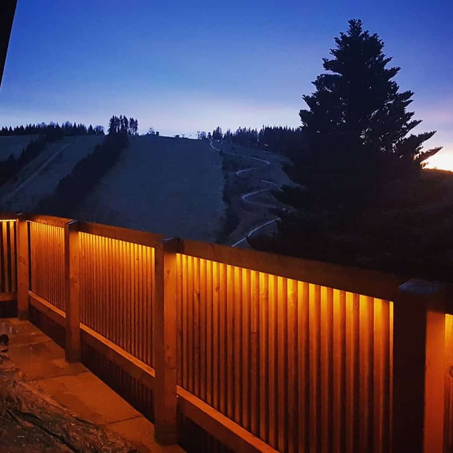 Cozy wooden balcony with warm under-rail lighting, offering a stunning twilight view of rolling hills and a winding trail