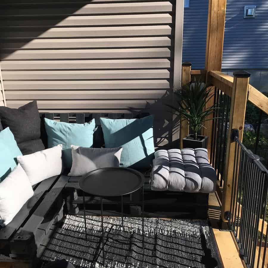 Cozy patio with a black pallet sofa, assorted pillows, a small round table, and a potted plant on a patterned rug