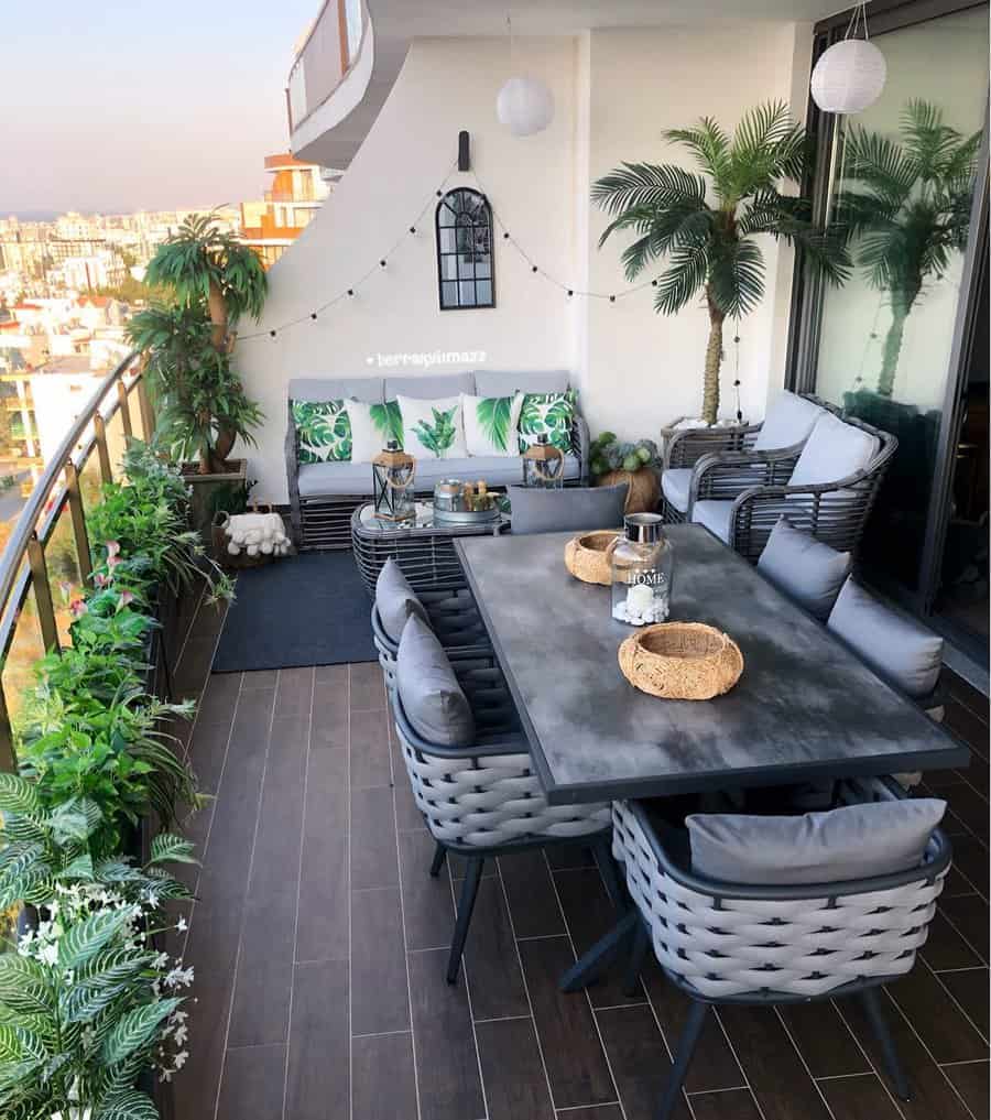 Stylish balcony with a dining table, chairs, sofas, potted plants, and city view featuring decor with pillows and string lights